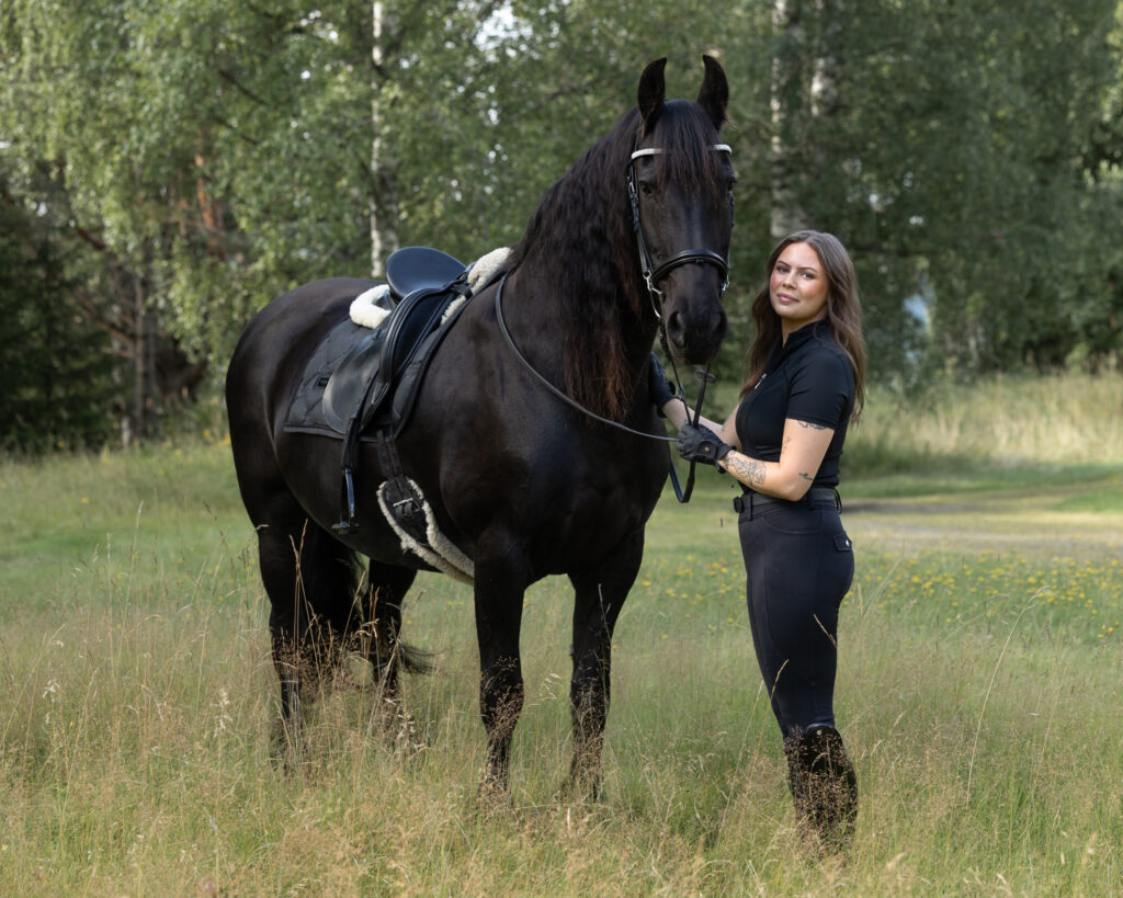 Kvinna med sin svarta häst på en sommaräng